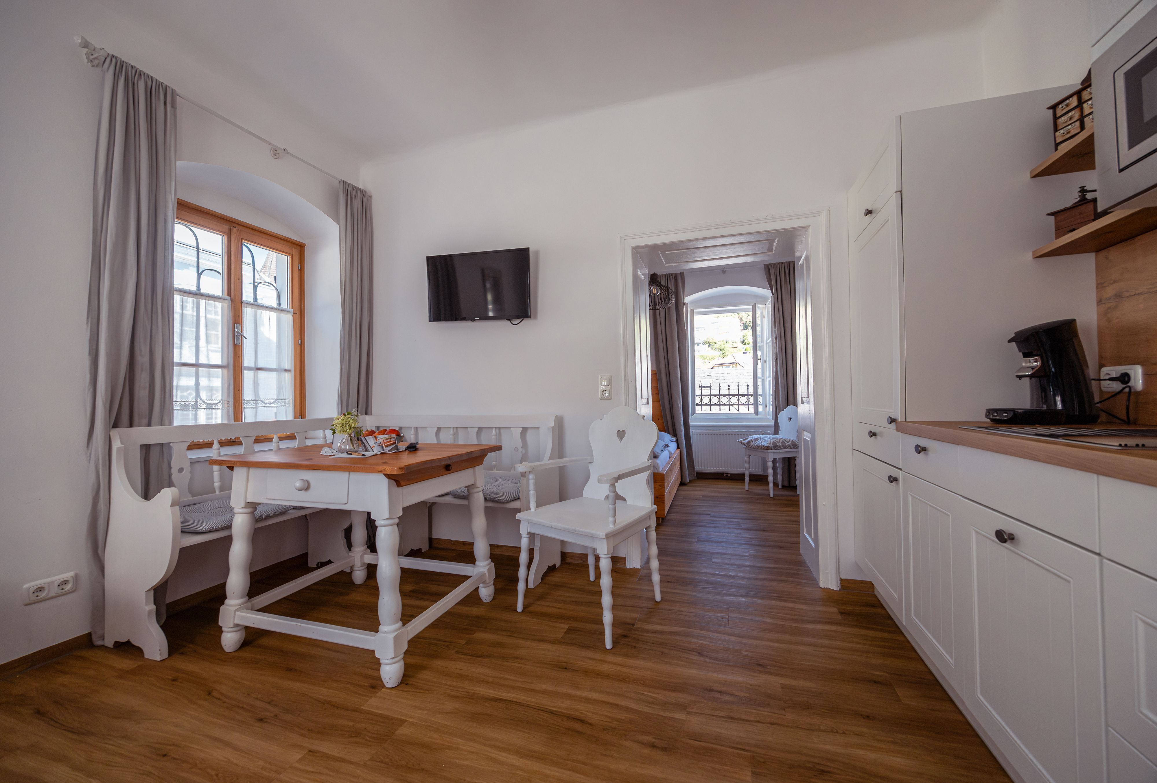 Světlý, útulný pokoj s dřevěnou podlahou, jídelním stolem, židlemi a kuchyňským koutem.