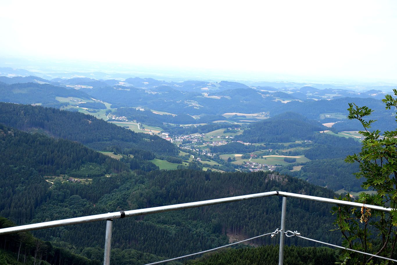 Pohled z kamenné zdi hradu na kopcovitou krajinu s lesy a vesnicemi.