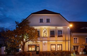 Hostinec svatého Floriána za soumraku s osvětlenou fasádou a sochou.