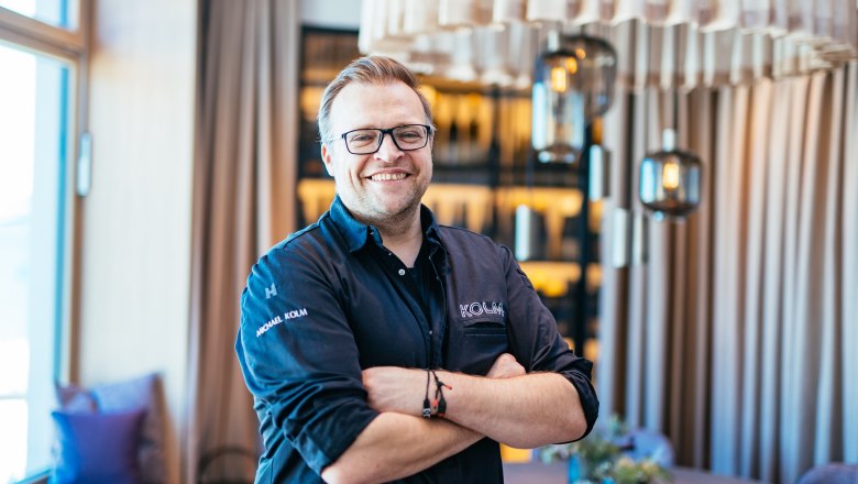 Usměvavý muž v oděvu šéfkuchaře stojí se založenýma rukama ve stylové restauraci.