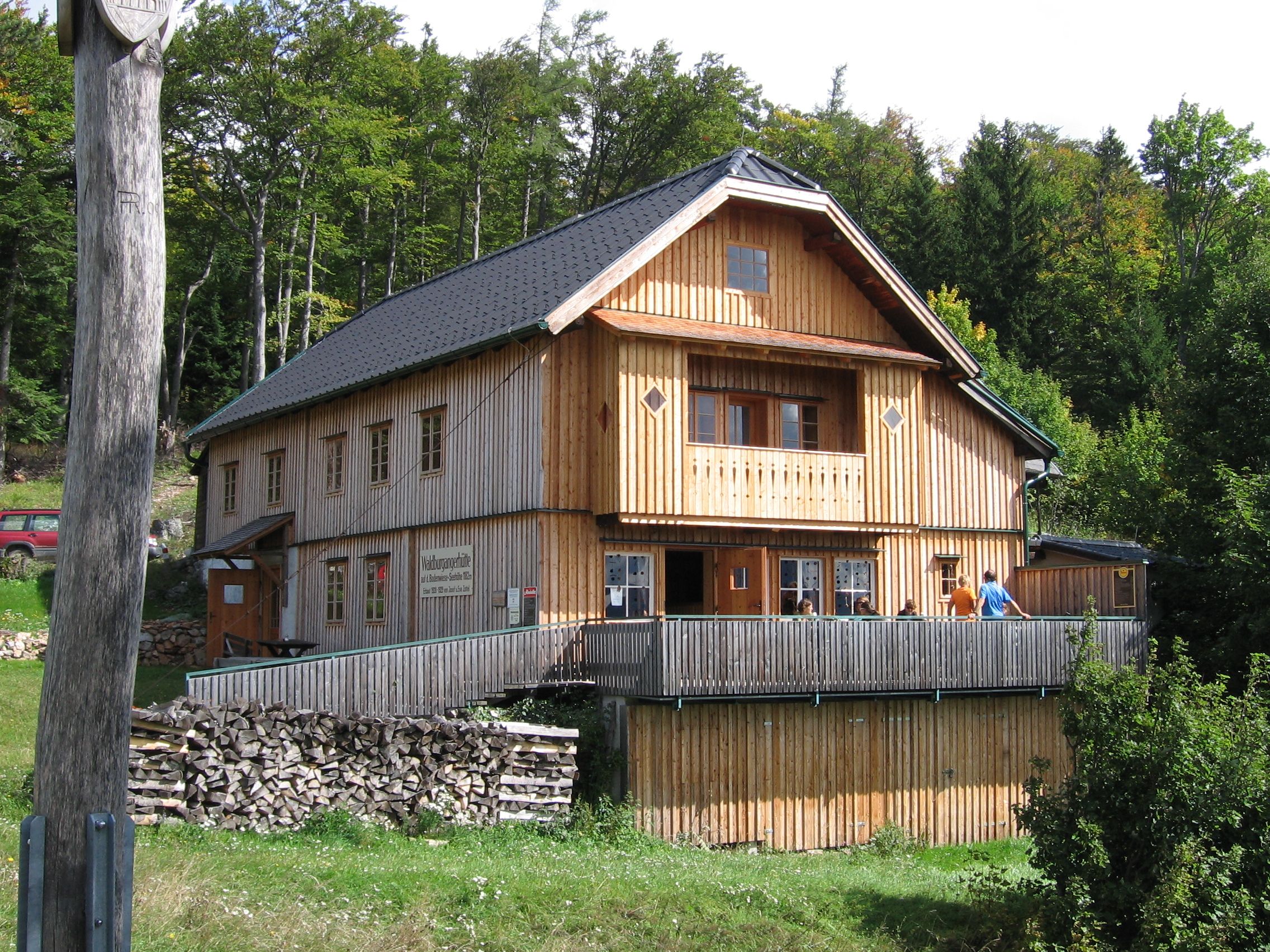 Dřevěná chata v lese s terasou a lidmi na ní.
