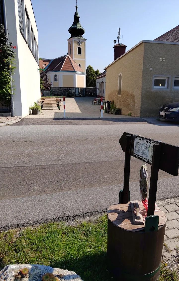 Vinný šenk Thaller Wolfsthal, pohled do vnitřního dvora se stoly s vínem, v pozadí je vidět kostel. 