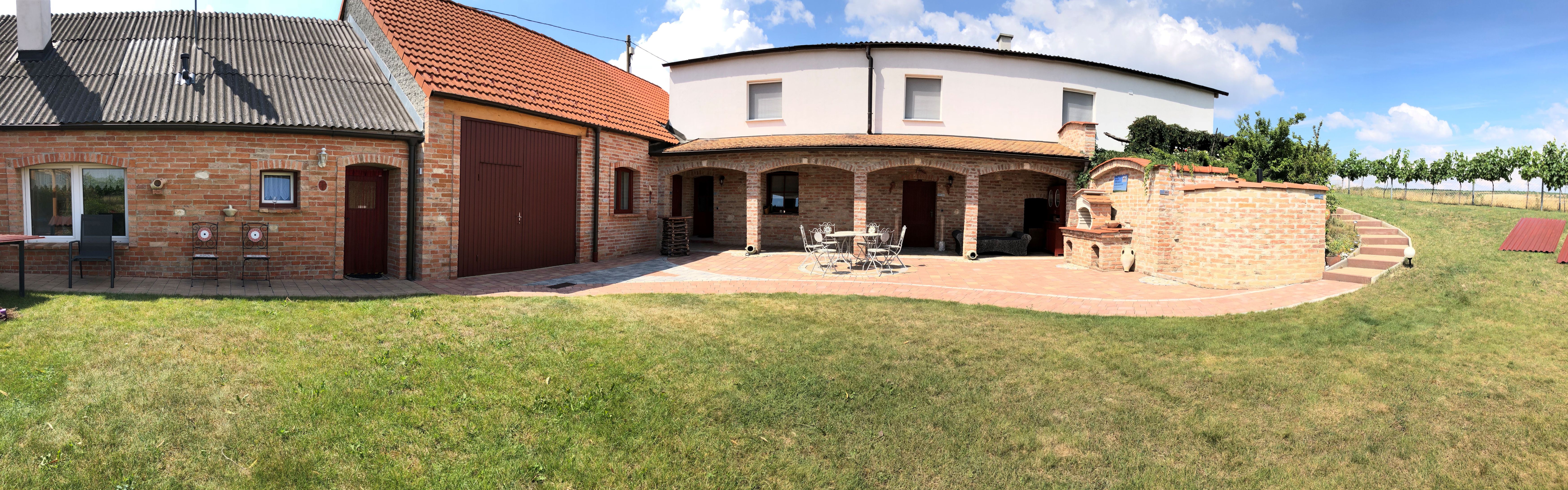 Zděná budova se zahradou a terasou za slunečného počasí.