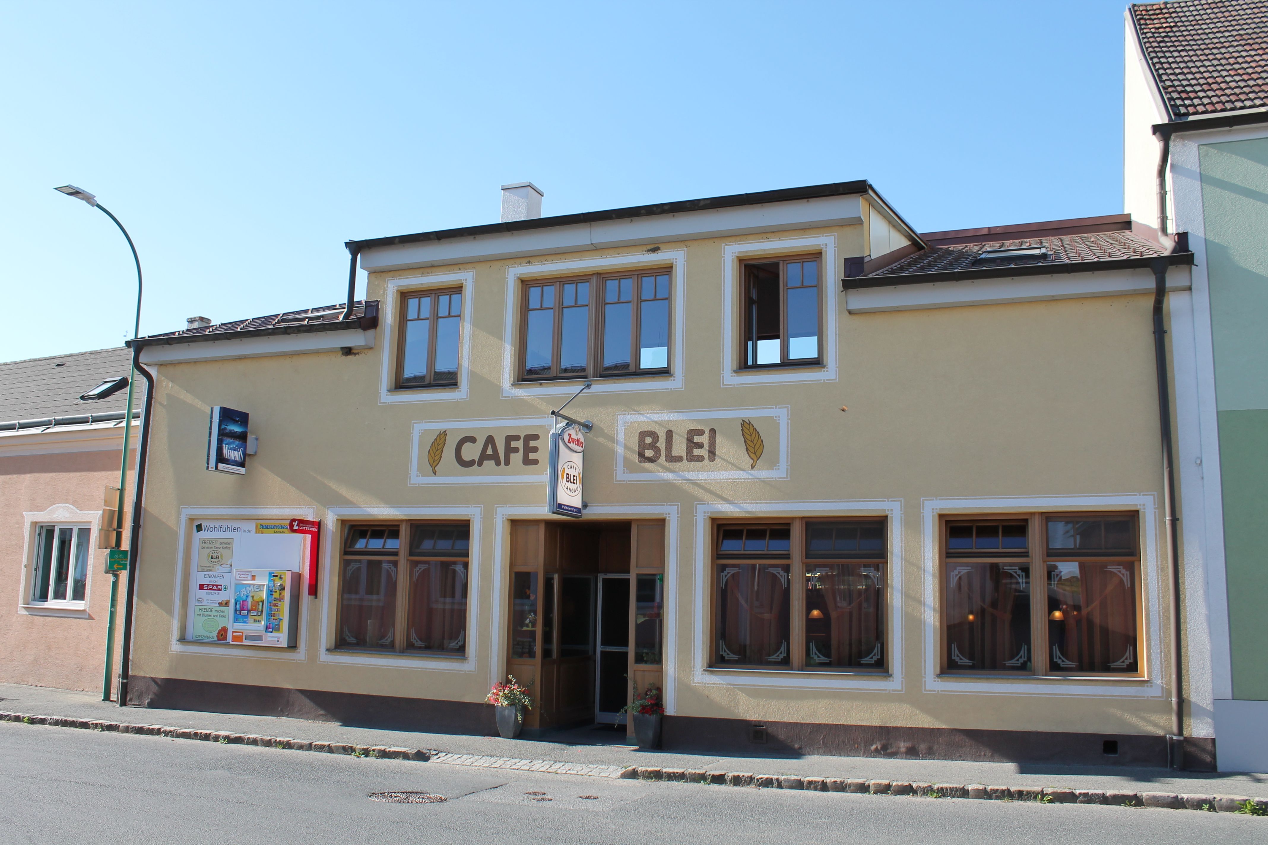 Pohled na kavárnu Café Blei se žlutou fasádou a velkými okny zvenčí.
