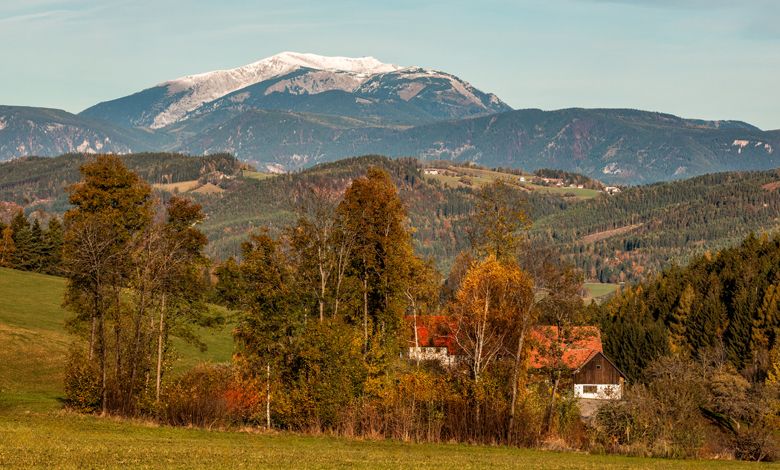 Podzimní krajina s horami, stromy a domem.