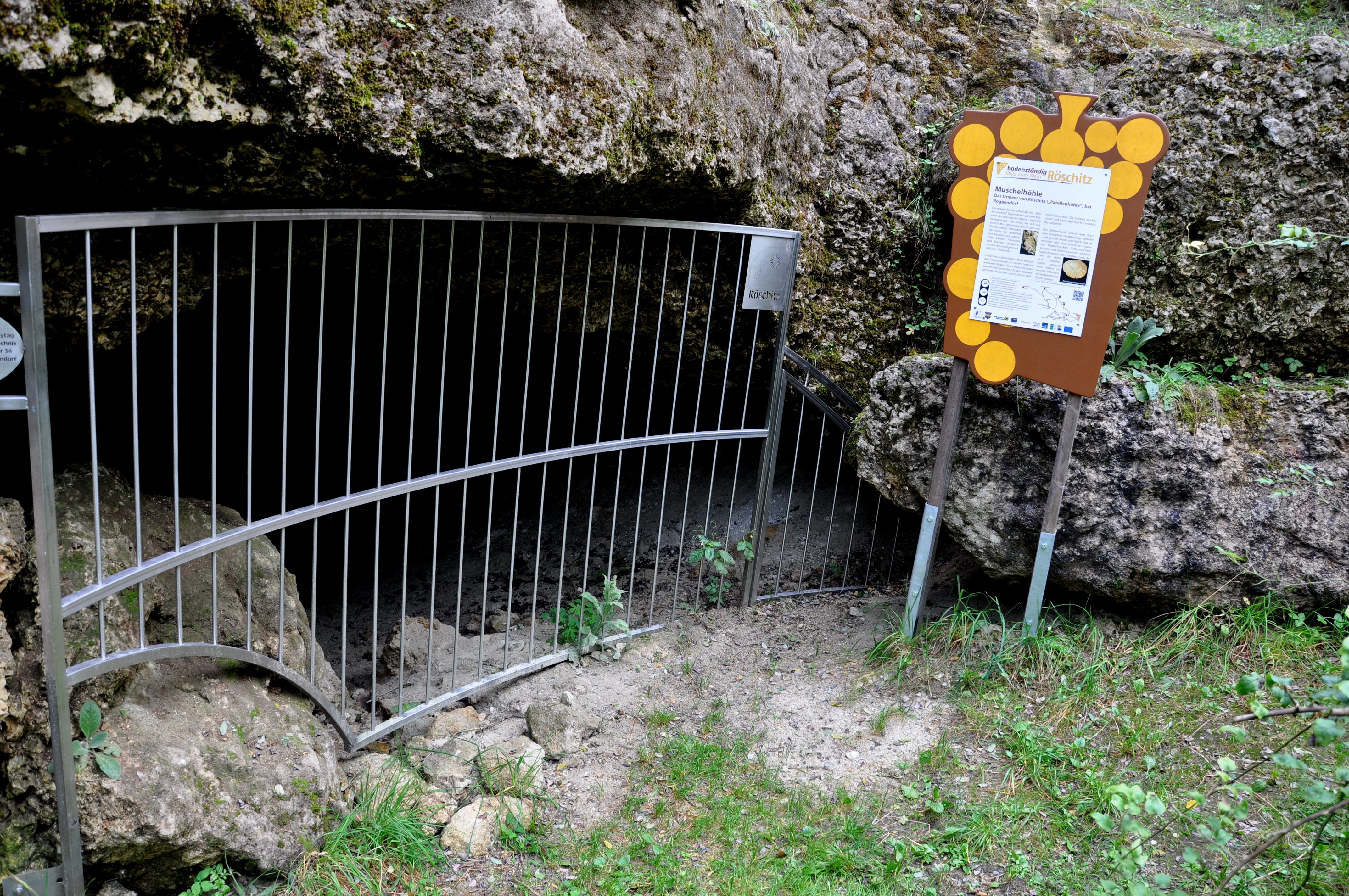 Vchod do Röschitzské mušlové jeskyně s mříží a informační tabulí.