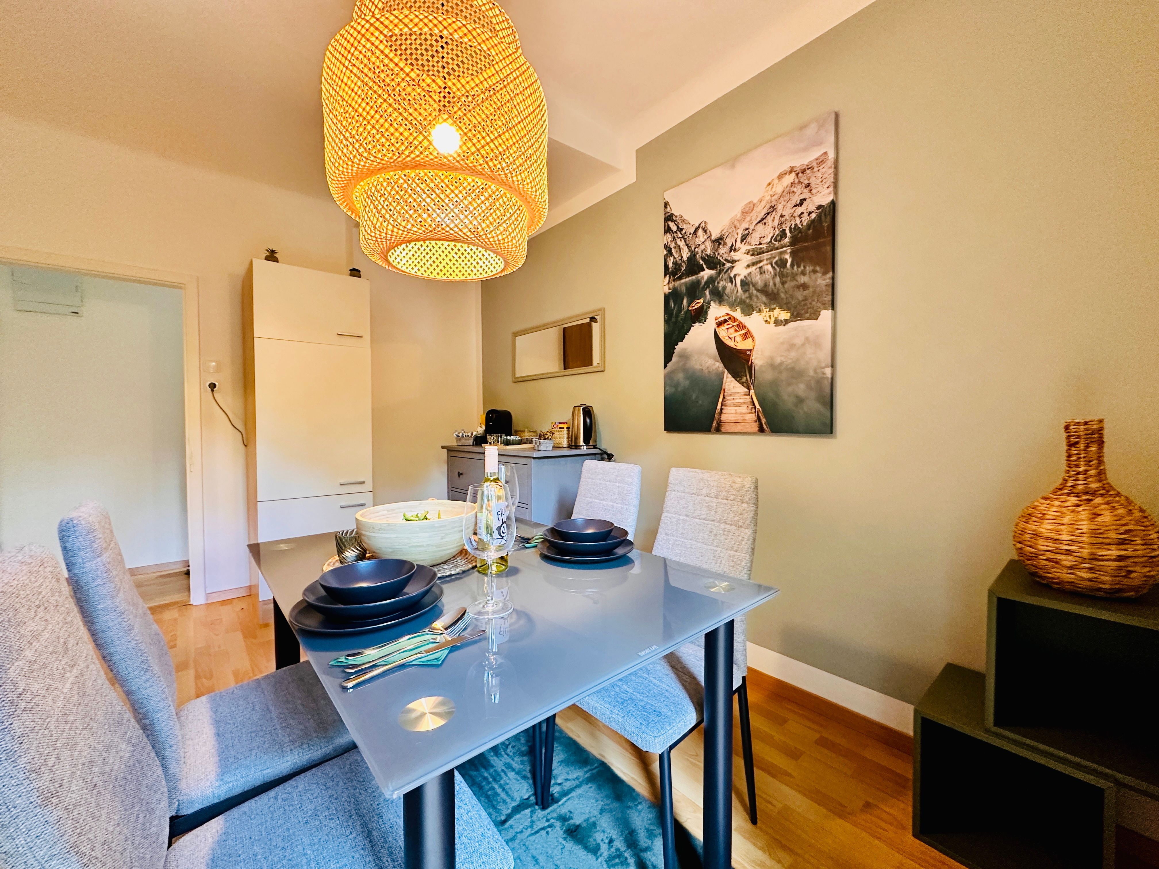 Jídelna se skleněným stolem, šedými židlemi a velkým stínidlem.