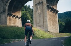 Ein Radfahrer gleitet mit Leichtigkeit auf einer kurvenreichen Straße, umgeben von majestätischen Brücken und üppigem Grün. Die frische Bergluft und die beeindruckende Landschaft laden dazu ein, die Schönheit der Natur in vollen Zügen zu genießen.