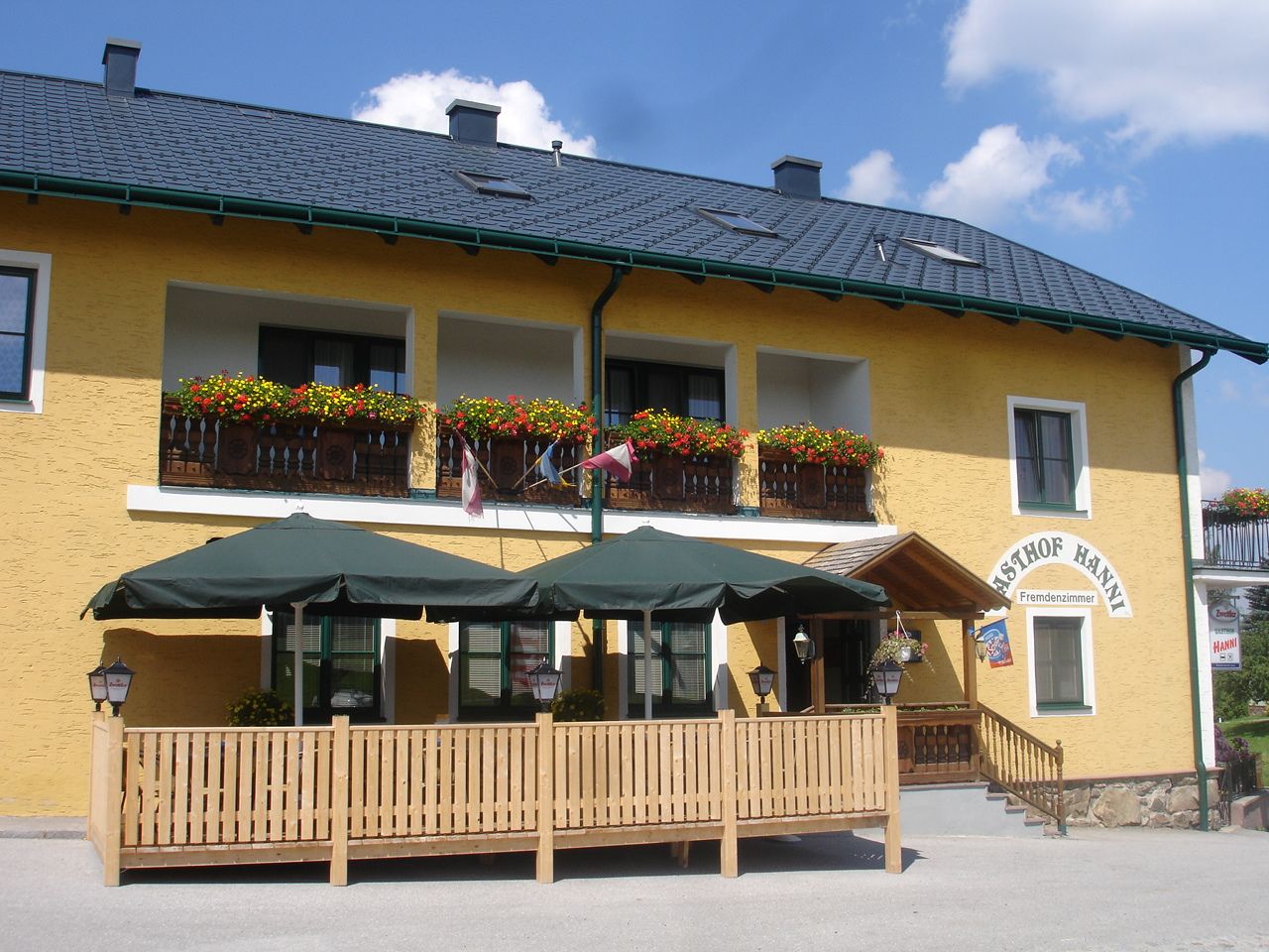 Žlutá budova s balkonem, květinami a terasou se slunečníky.