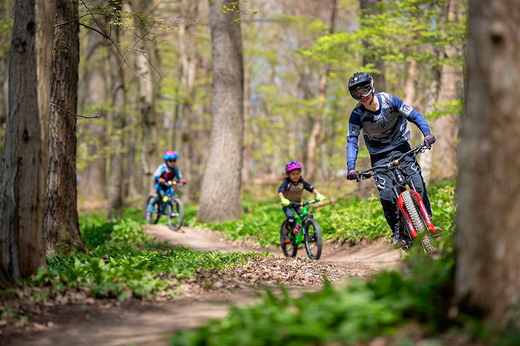 Tři horští cyklisté jedou po lesní cestě.