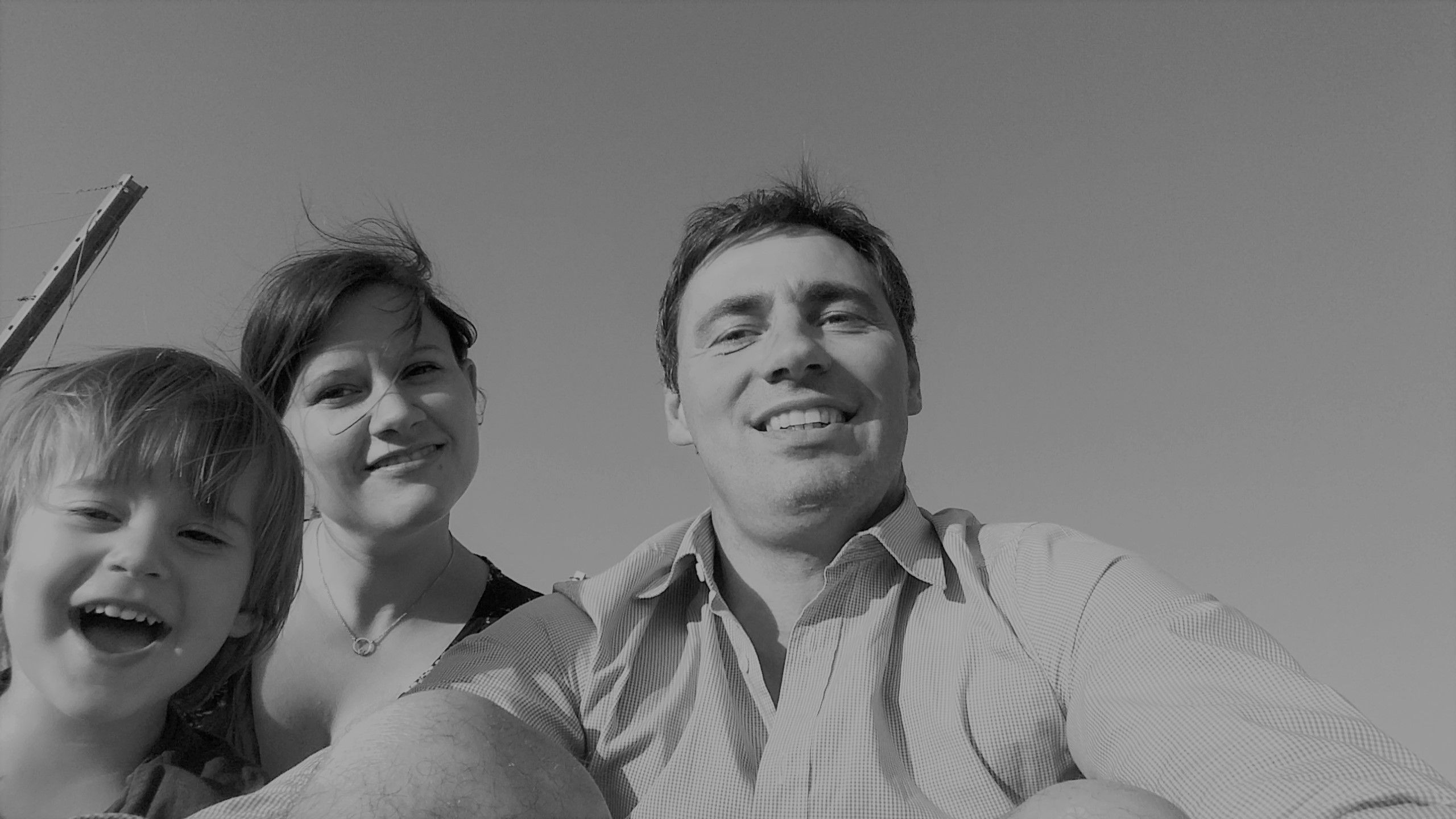 Černobílá fotografie usmívající se rodiny složené z muže, ženy a dítěte, kteří se dívají do fotoaparátu.