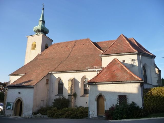 Historický kostel s červenou taškovou střechou a malou věží se zelenou střechou.