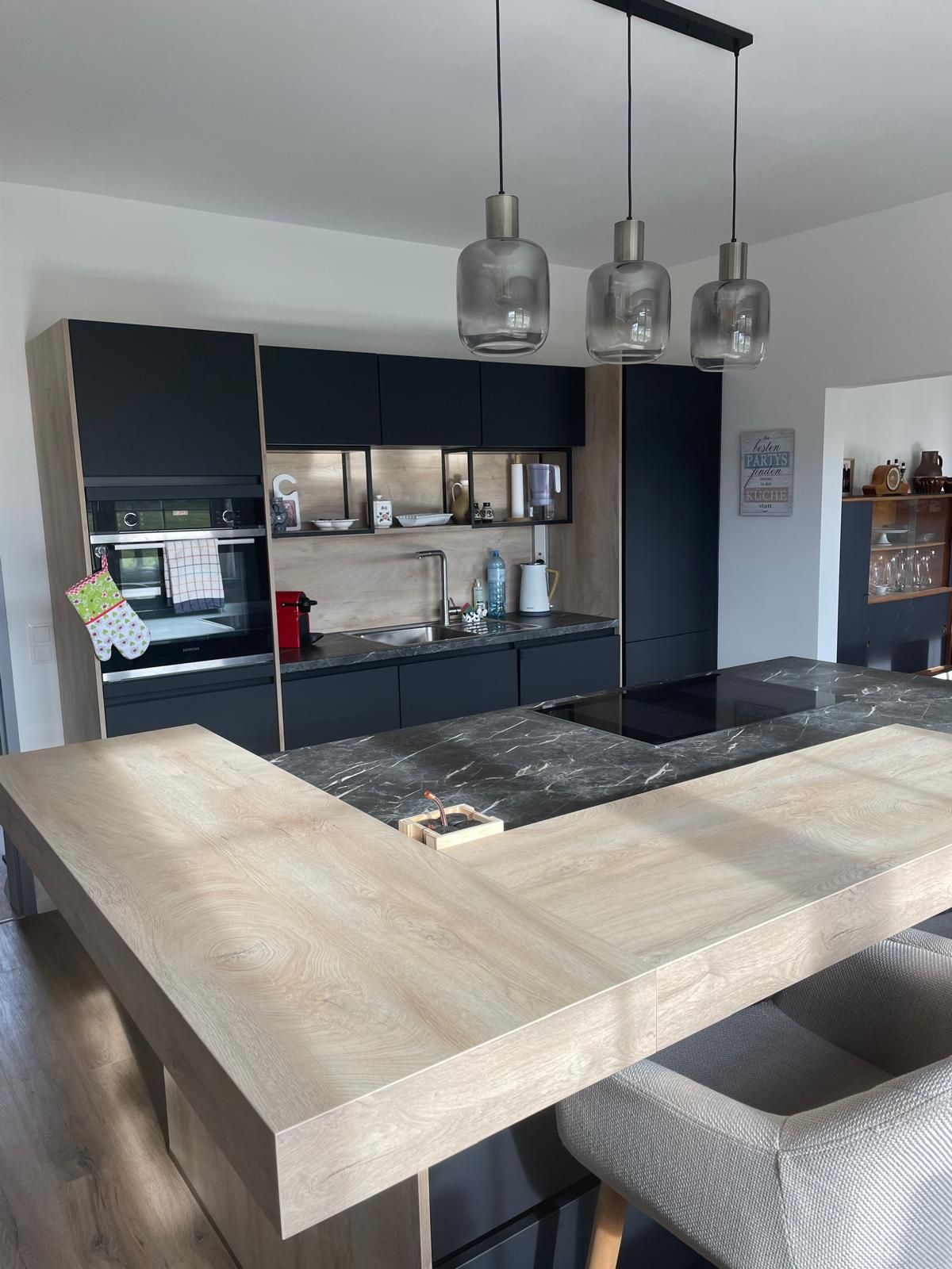 Moderní kuchyně s dřevěnými a mramorovými prvky, třemi závěsnými lampami a černými skříňkami.