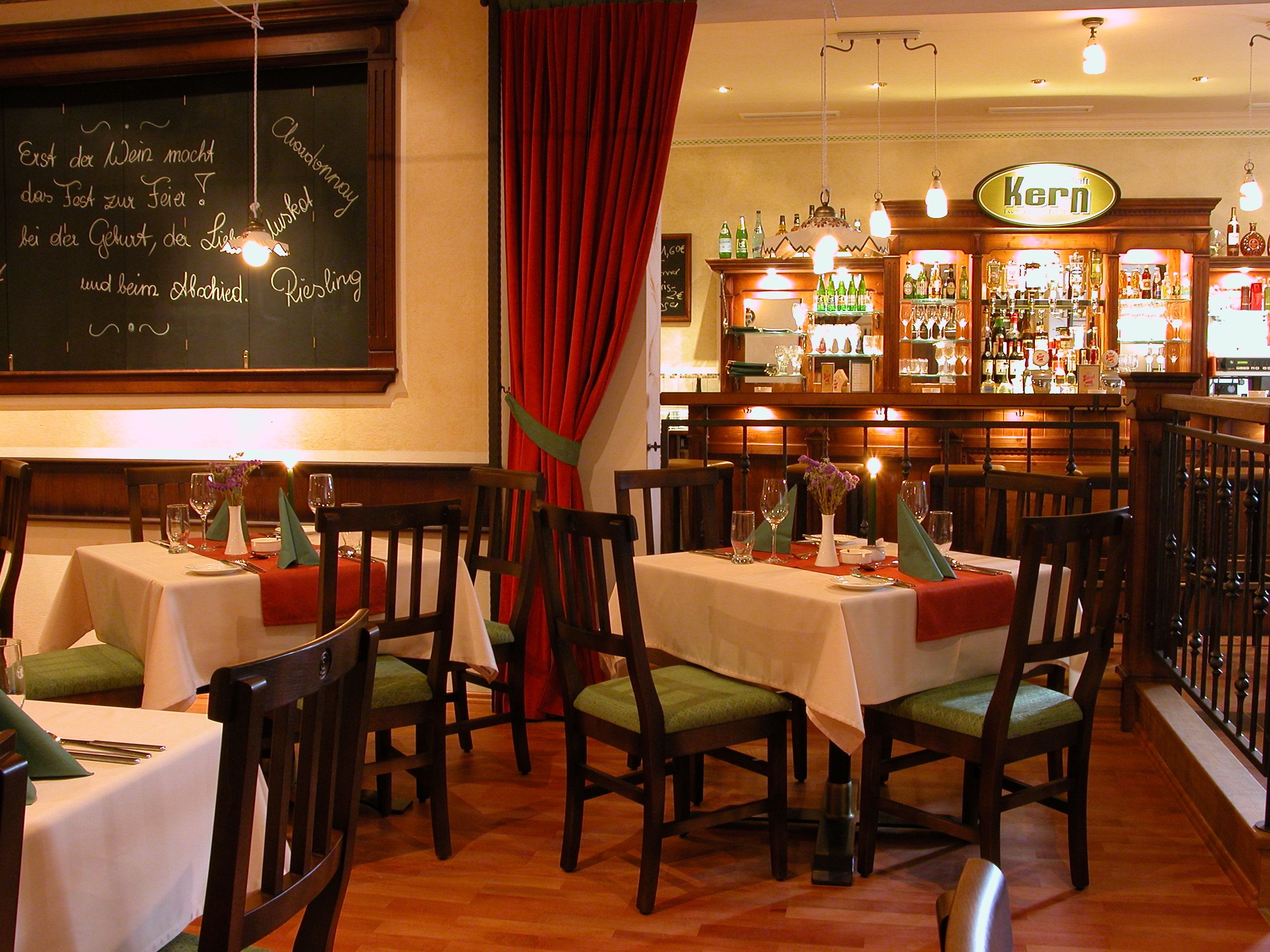 Útulná restaurace s dřevěným nábytkem, prostřenými stoly a barem v pozadí.