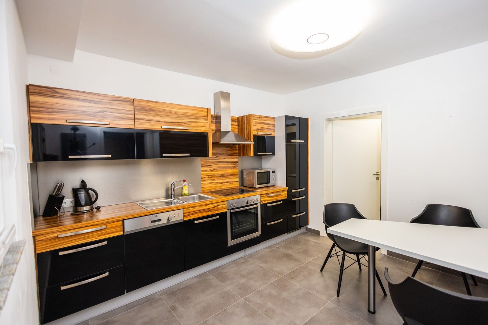 Moderní kuchyně s dřevěnými a černými lesklými deskami, jídelním stolem a židlemi.