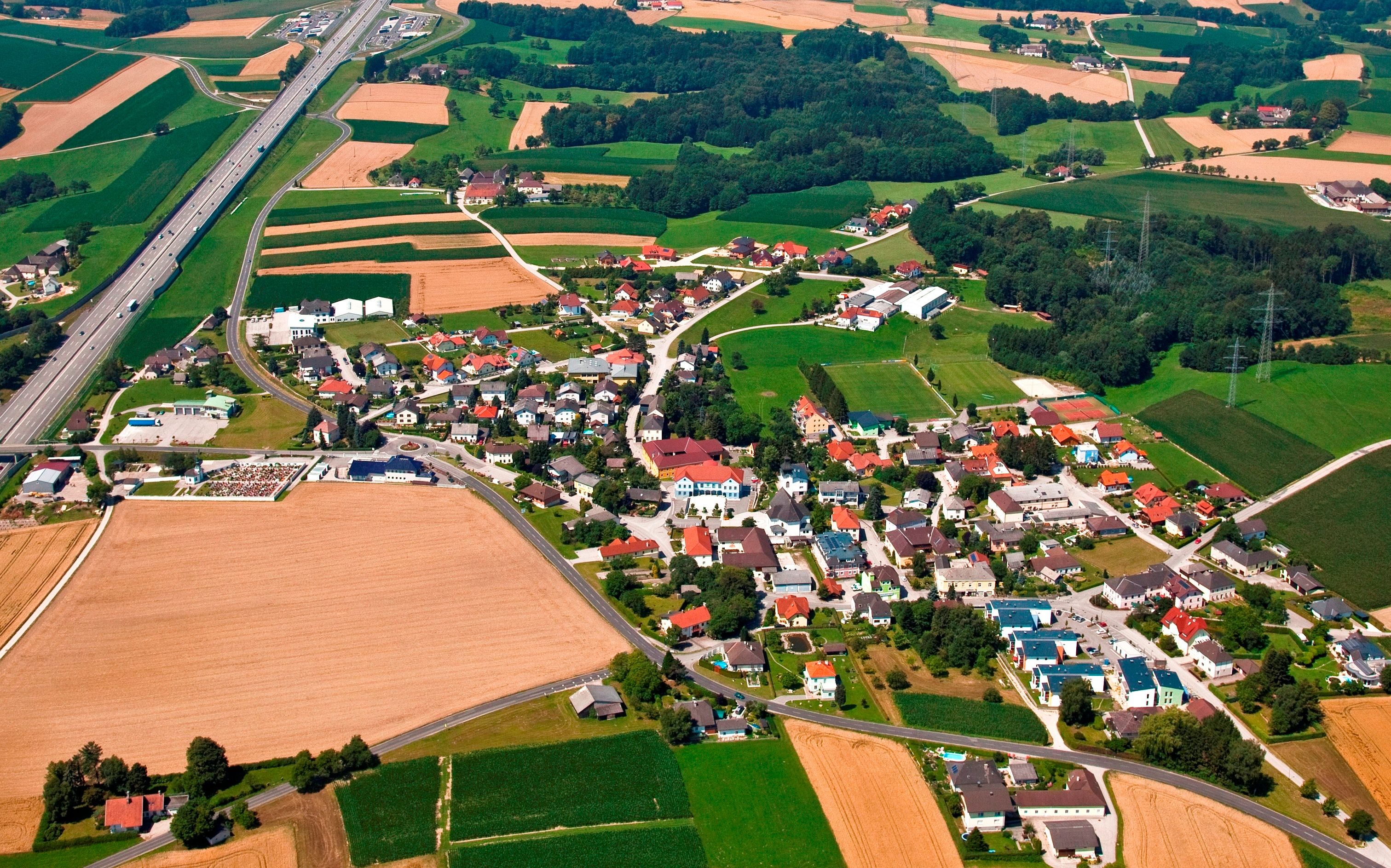 Letecký pohled na vesnici s poli a dálnicí.