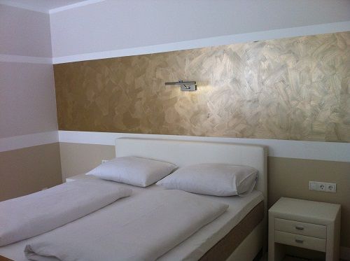 Moderní ložnice s manželskou postelí a zlatou výzdobou stěn.