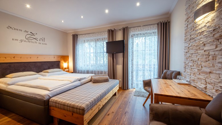 Útulná ložnice s manželskou postelí, dřevěným nábytkem a kamennou stěnou.