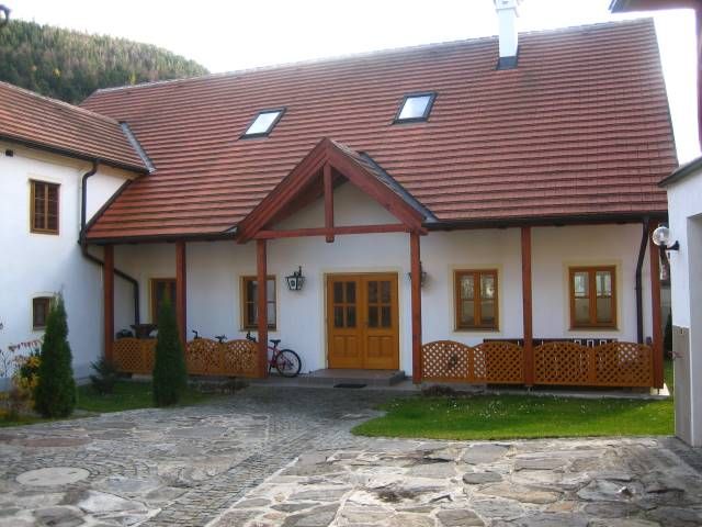 Tradiční budova s červenou taškovou střechou a dřevěnými prvky, obklopená dlážděným nádvořím.