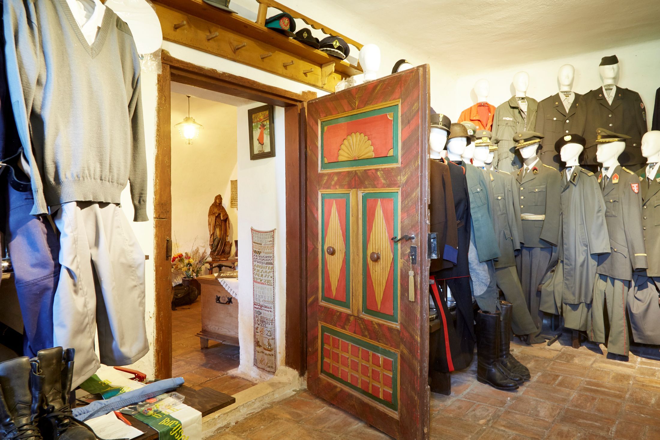 Pohled do interiéru místnosti se starými uniformami a barevně natřenými dřevěnými dveřmi.