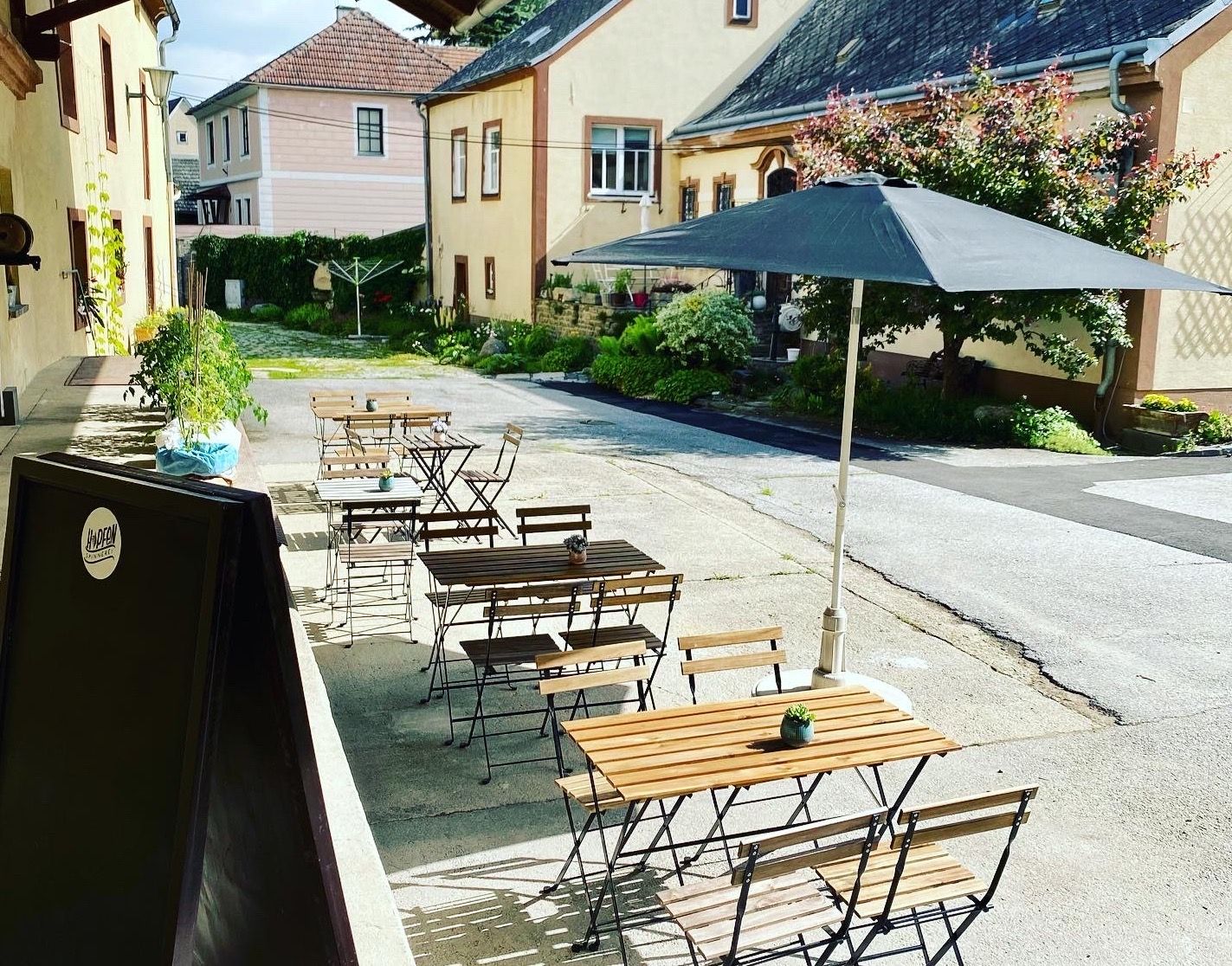Zahrada pro hosty s dřevěnými stoly a židlemi, slunečníkem a rostlinami ve vnitřním dvoře.