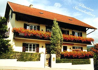 Dvoupatrový dům s červenými květinami na balkonech, označený "Pension Steinkellner".