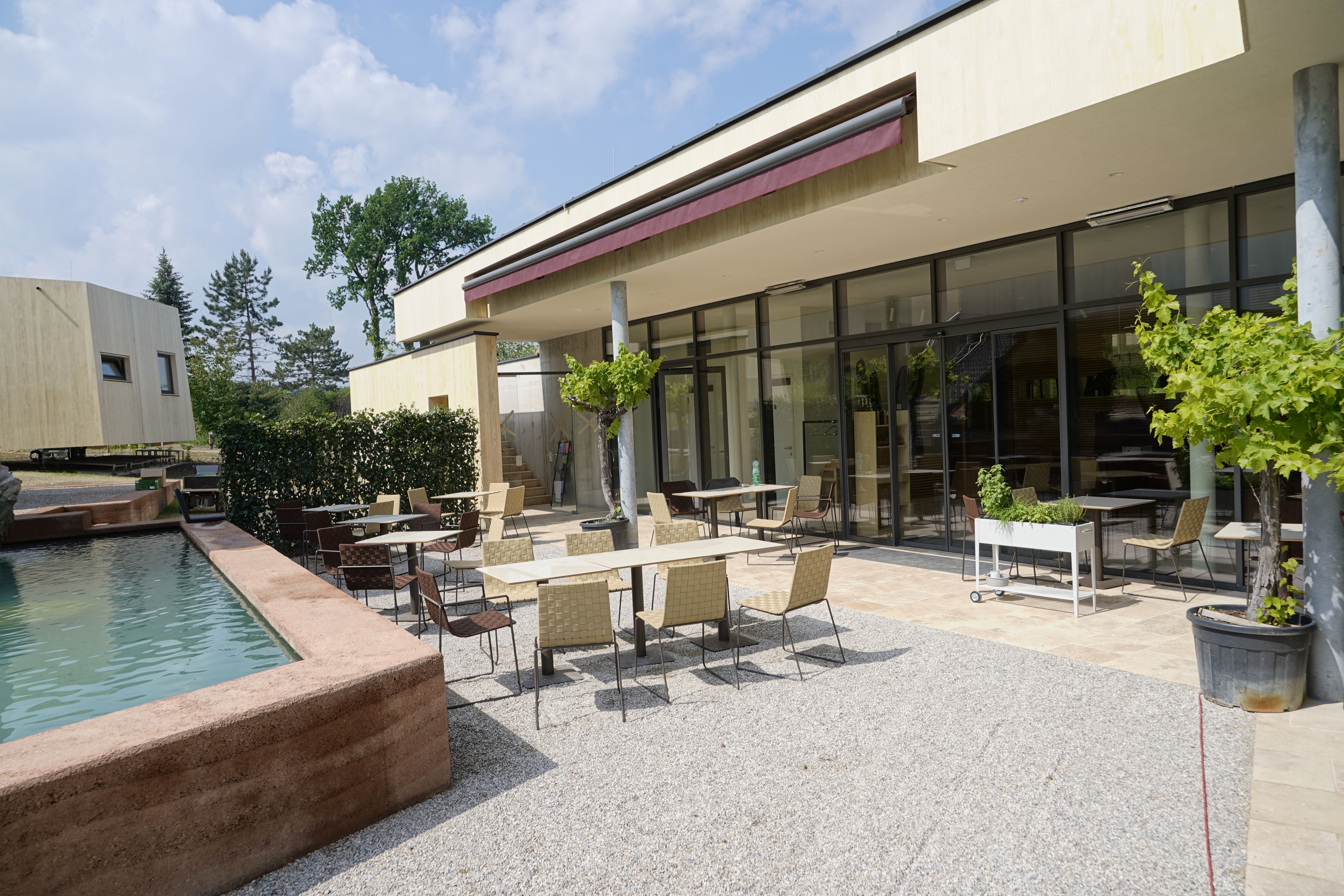 Venkovní prostor moderní snídaňové restaurace se stoly a židlemi na terase u vodní nádrže.