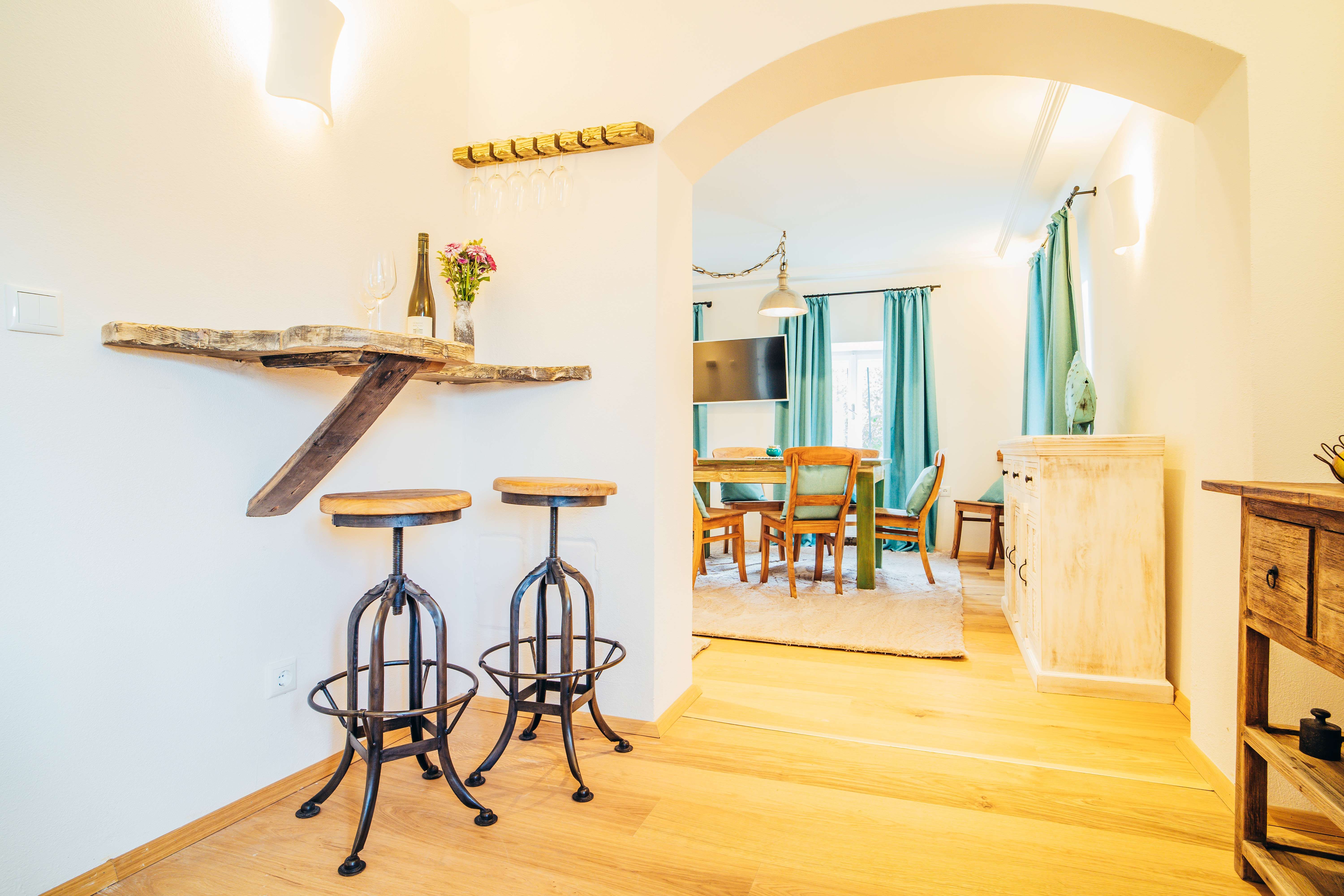 Útulný obývací pokoj s dřevěným nábytkem, barovými stoličkami a jídelním stolem.