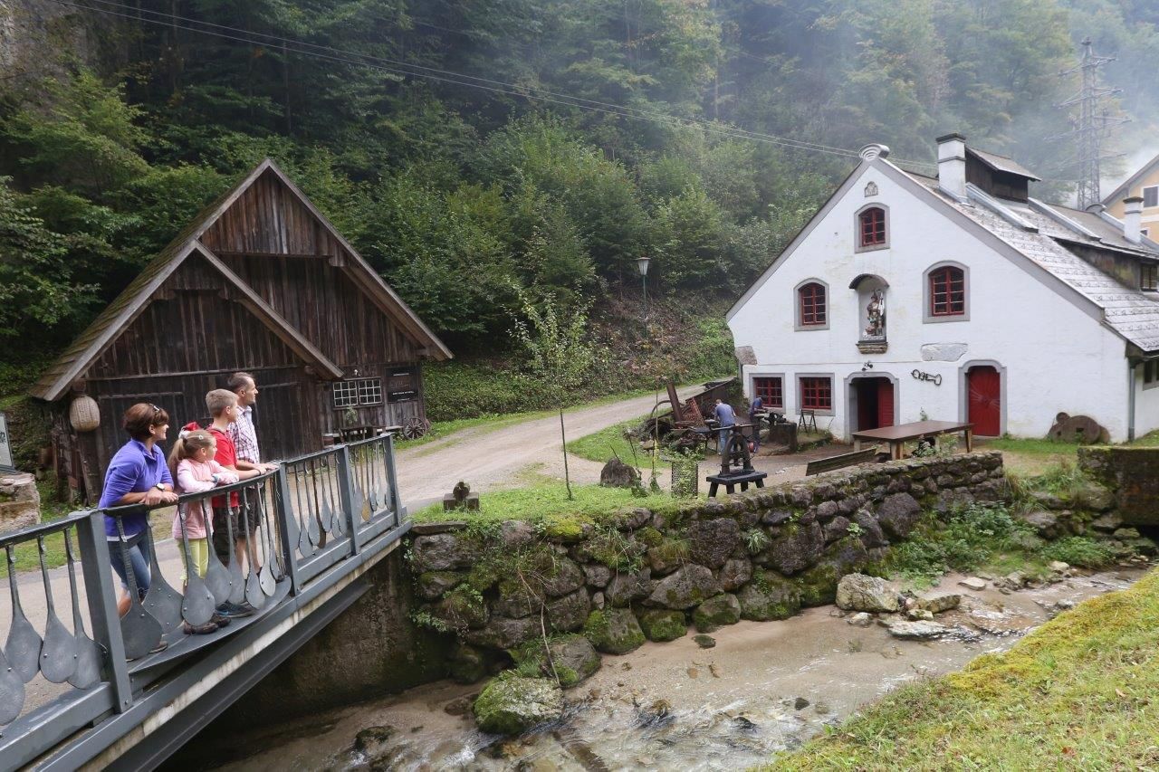 Rodina stojí na mostě před historickou budovou na venkově.