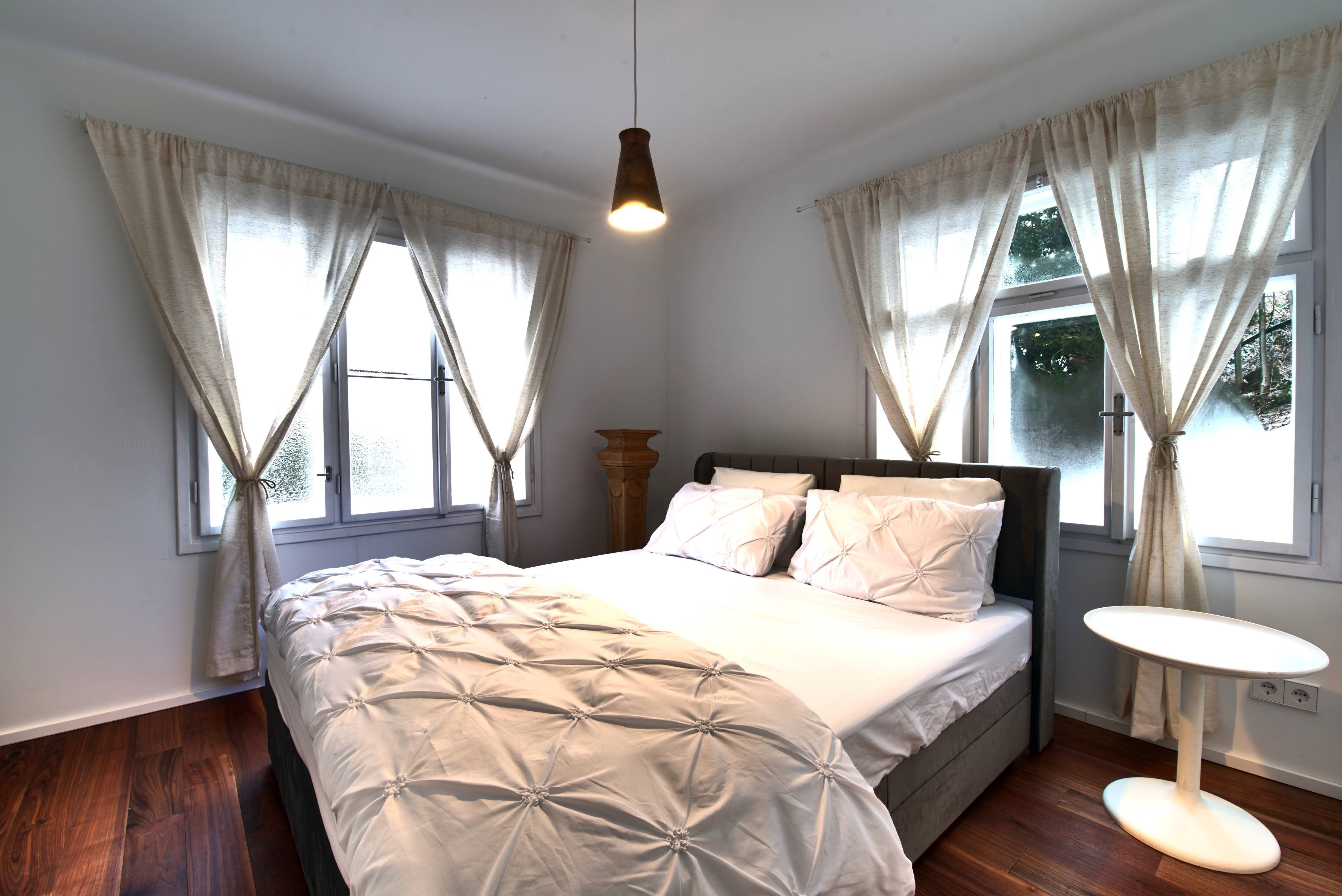 Útulná ložnice s velkou postelí, bílými závěsy a malým kulatým stolkem.