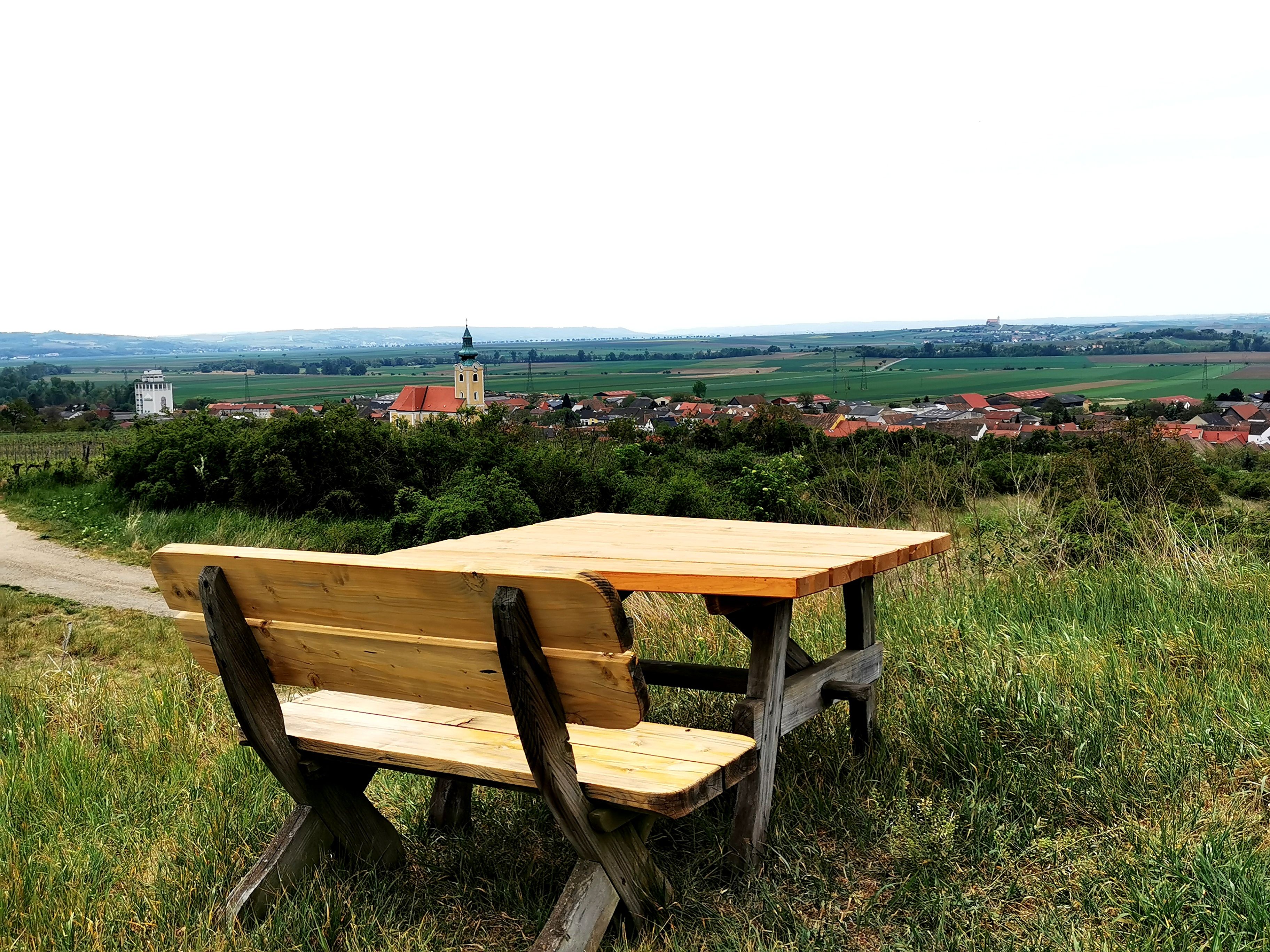 Dřevěná lavička se stolem na kopci s výhledem na Röschitz a okolní krajinu.