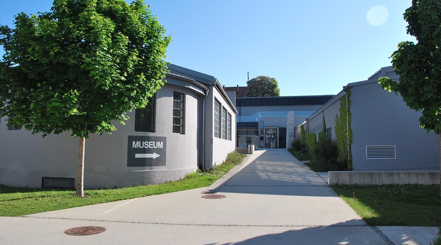 Vchod do muzea MAMUZ v Mistelbachu s rozcestníkem a stromy.