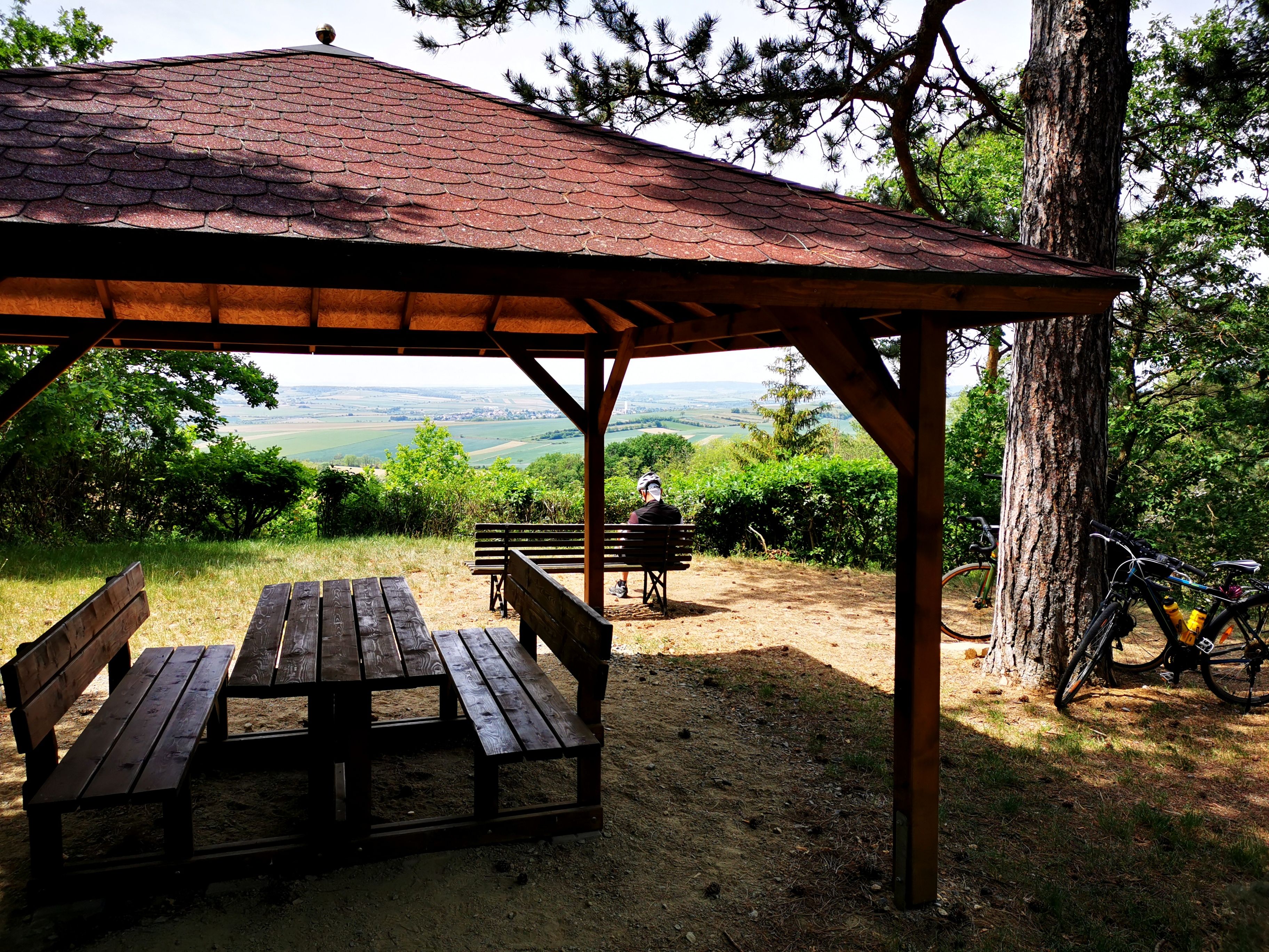 Dřevěný pavilon se stolem a lavicemi, výhled na vinice, kolo na stromě.