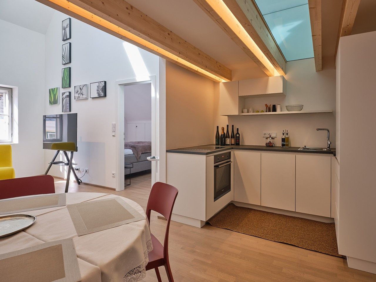 Moderní kuchyně s dřevěnými trámy, jídelním stolem a výhledem do ložnice.