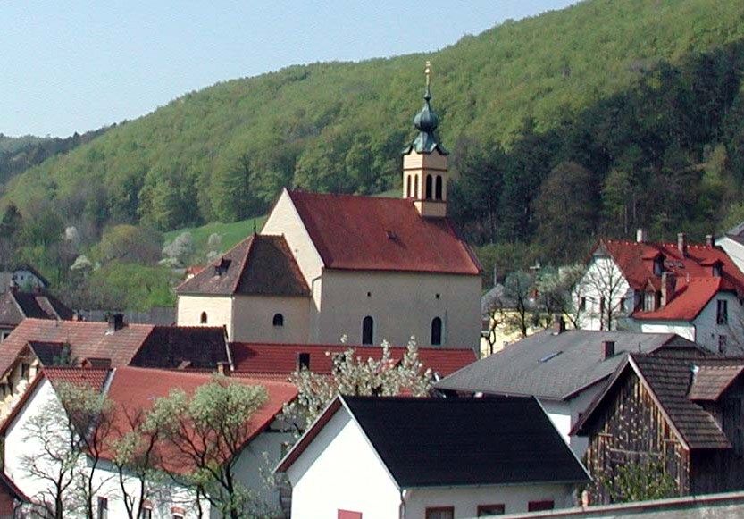 Poutní kostel Maria Raisenmarkt ve venkovském prostředí s kopci v pozadí.