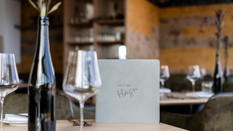 Prostřený stůl v restauraci se sklenicemi na víno, lahví vína a jídelním lístkem.