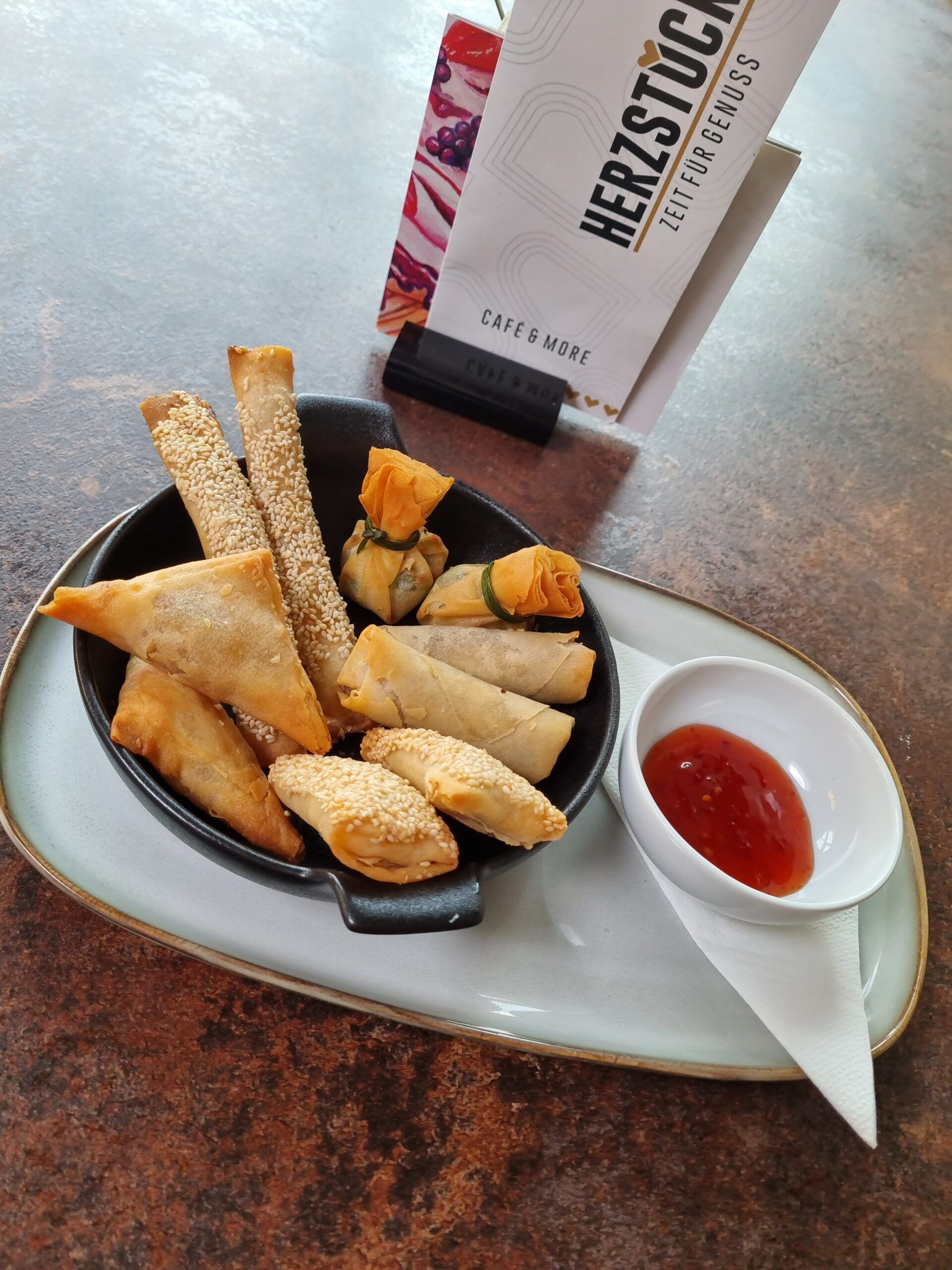 Různé smažené občerstvení na talíři s dipem a kavárenským menu v pozadí.