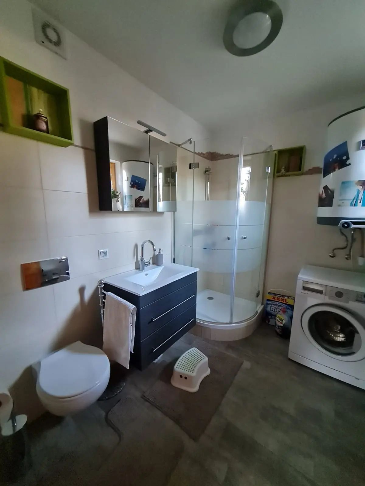 Moderní koupelna se sprchovým koutem, umyvadlem, toaletou a pračkou.