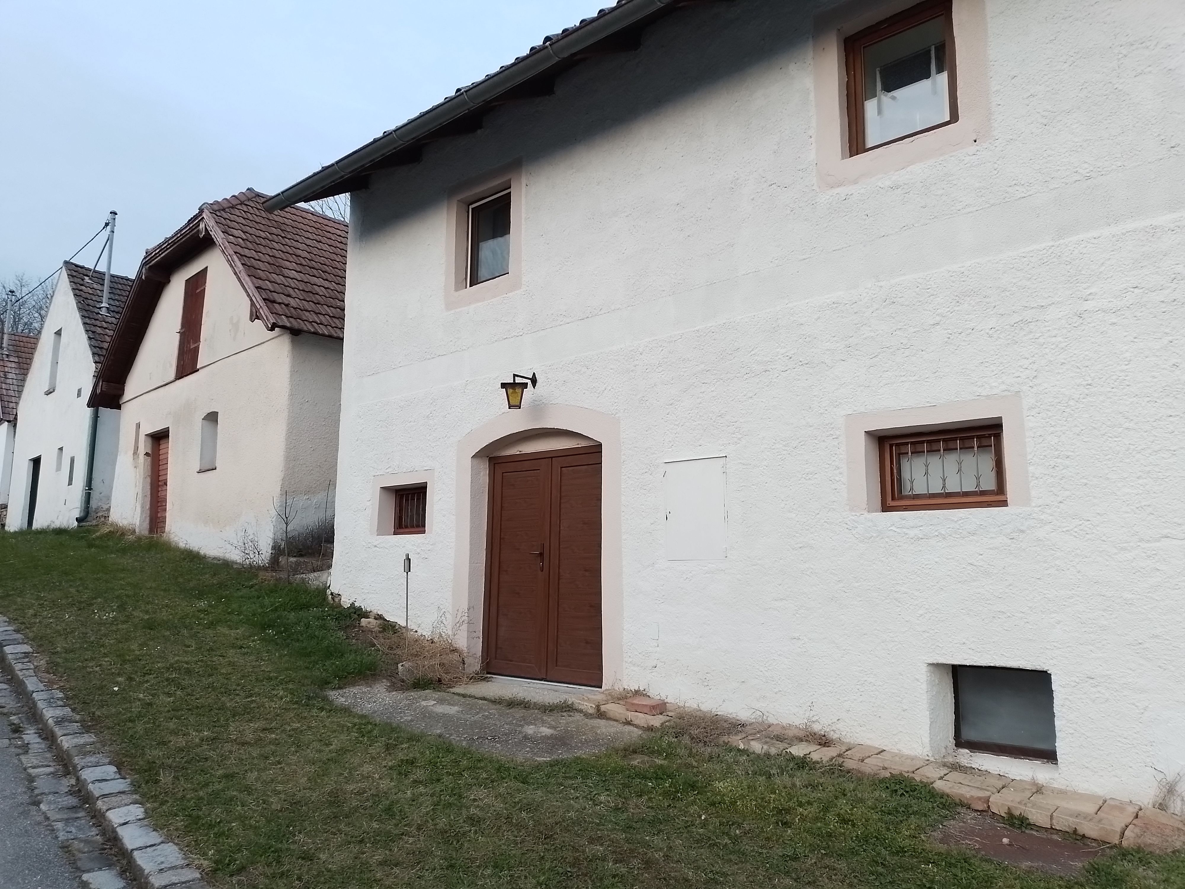 Řady bílých domů s hnědými dveřmi a okny podél silnice s travnatými okraji.