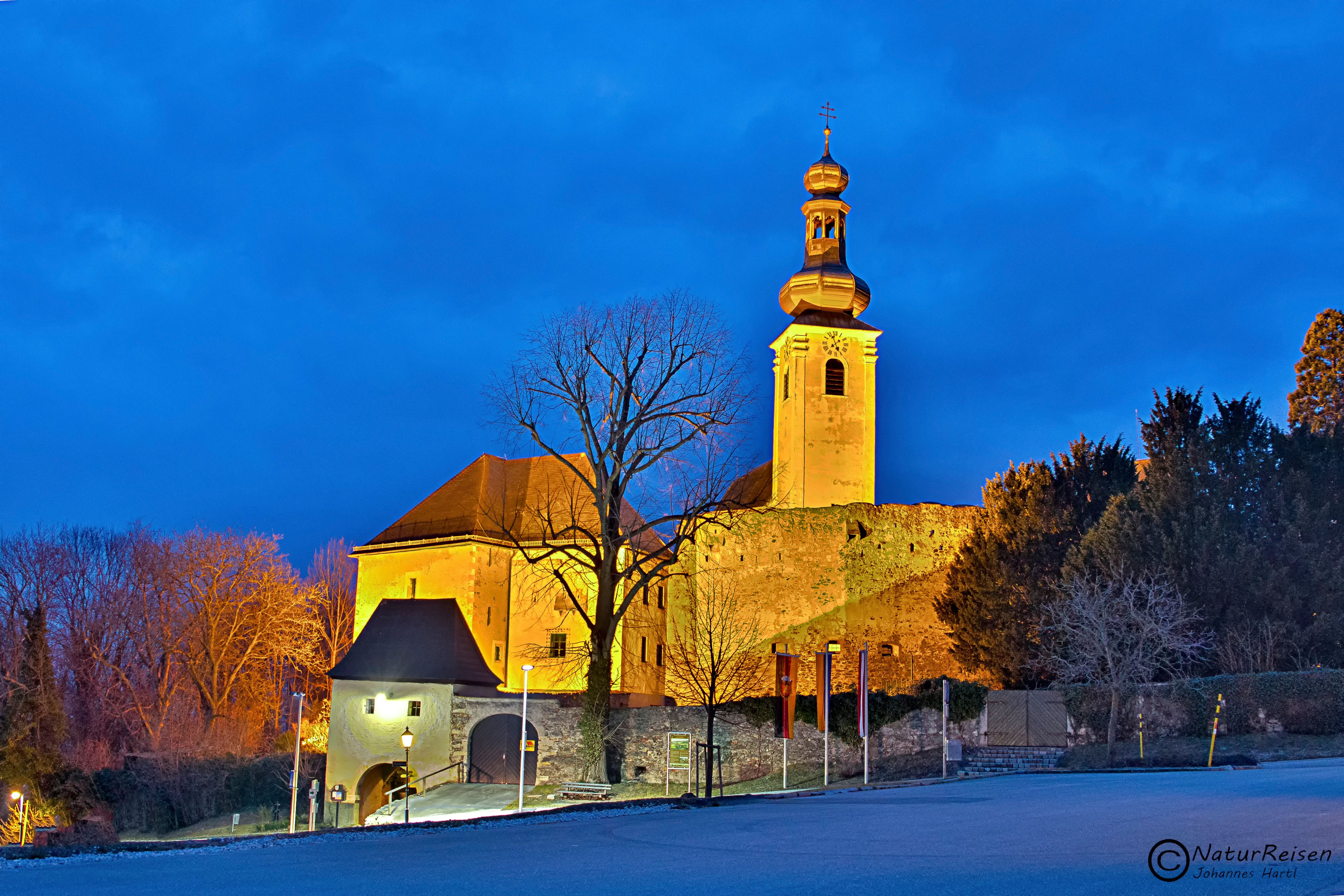 Osvětlený hrad Gloggnitz za soumraku s modrou oblohou.