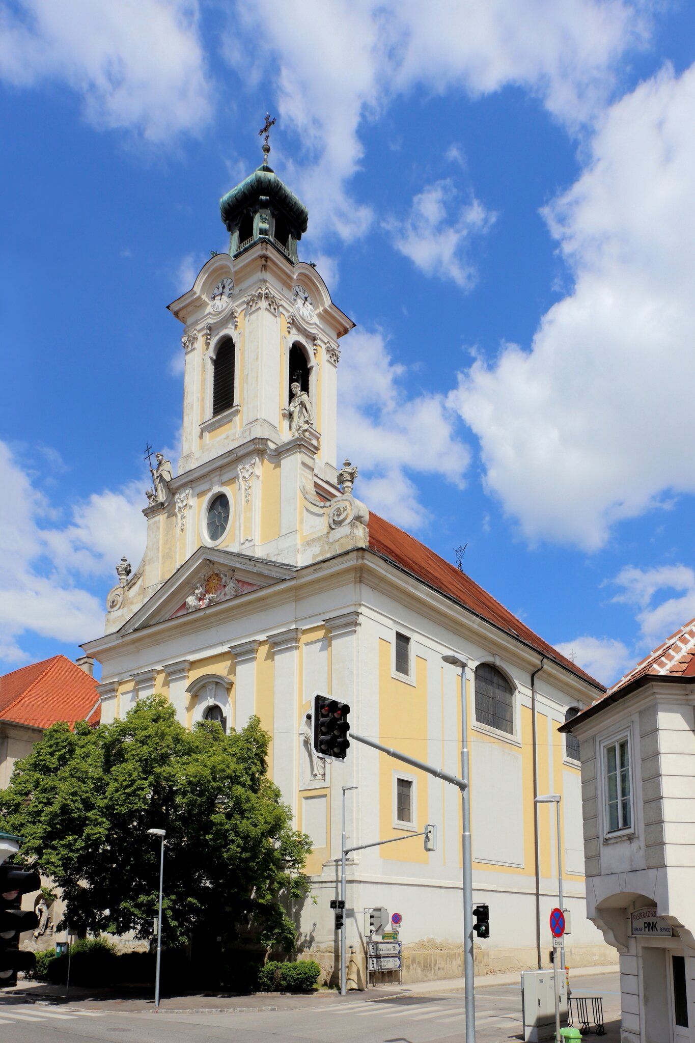 Barokní kostel s věží a hodinami na pozadí modré oblohy.