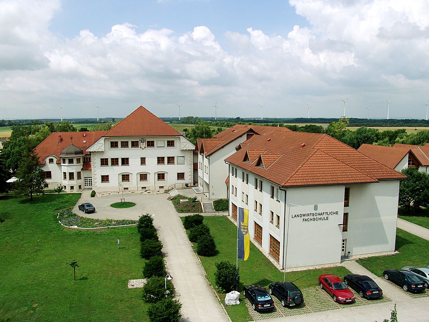 Letecký pohled na komplex školních budov s červenými střechami a okolní zelení.