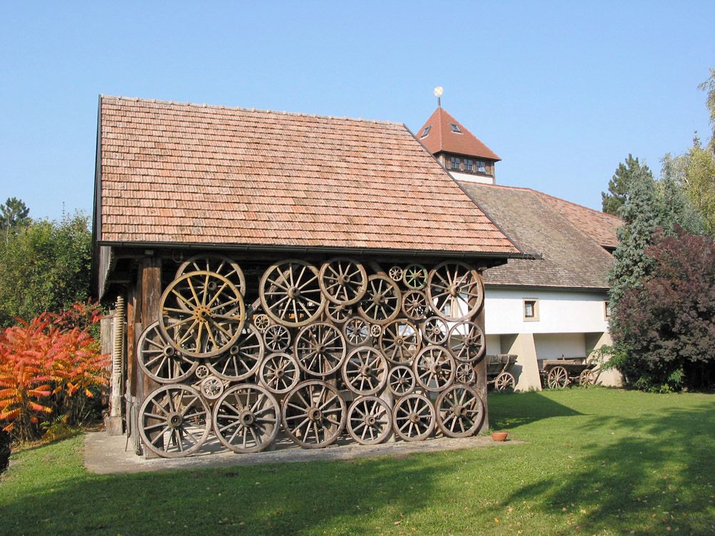 Budova s fasádou ze starých kol vozů, obklopená stromy a trávníkem.
