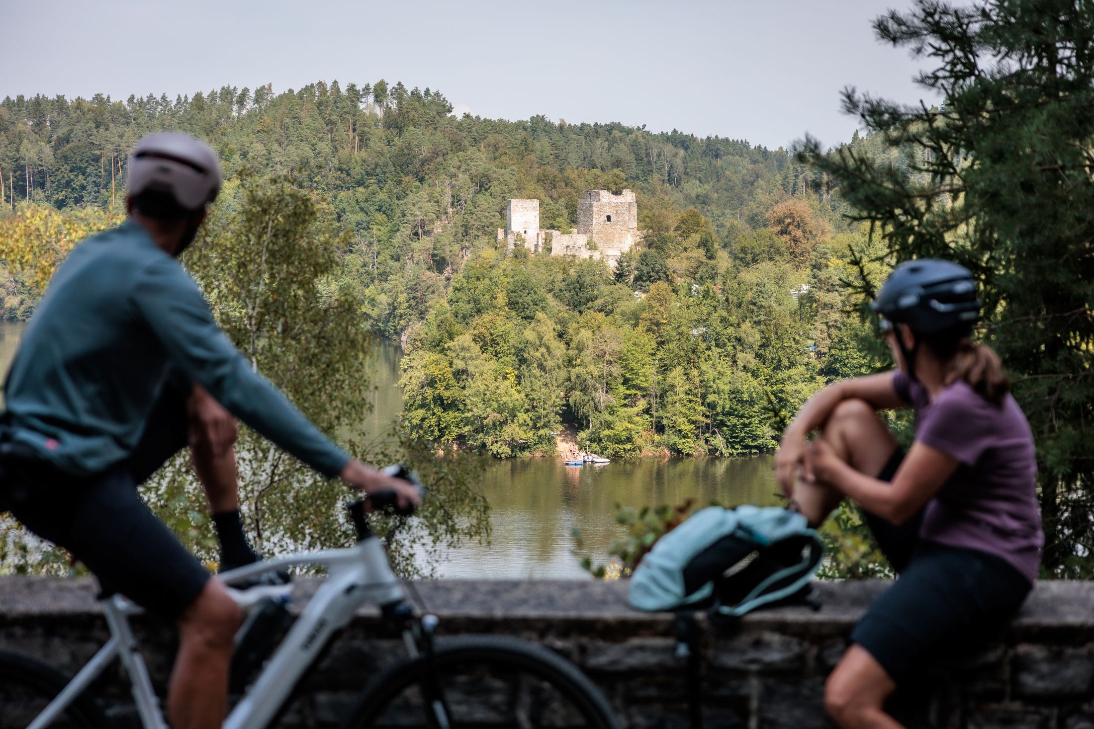 Dva cyklisté se dívají na zříceninu Dobra přes jezero.
