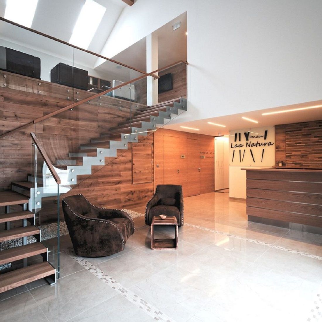 Moderní vstupní prostor s dřevěným obložením, schodištěm a recepcí.