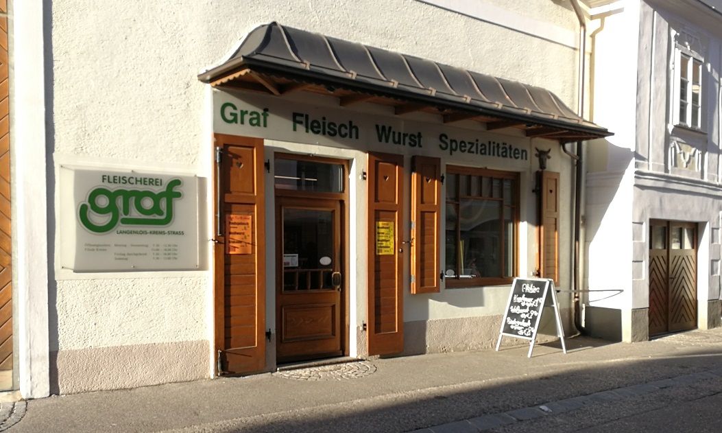 Pohled na řeznictví Graf zvenčí s dřevěnými dveřmi a reklamní tabulí.