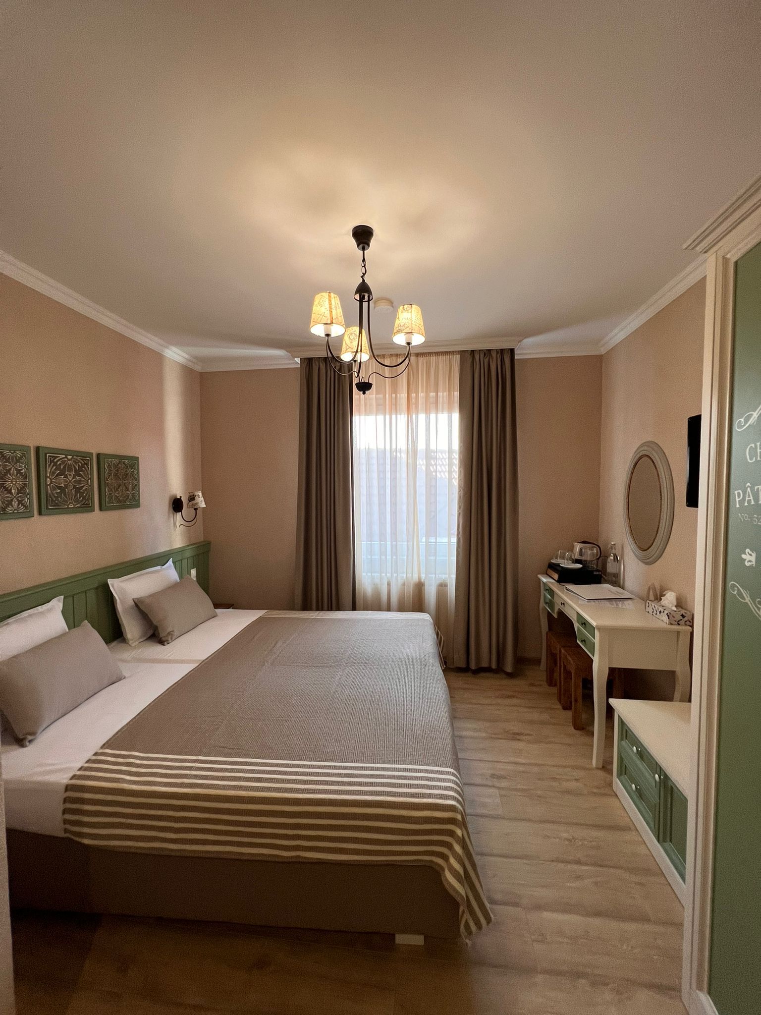 Útulný hotelový pokoj s manželskou postelí, psacím stolem a oknem se závěsy.