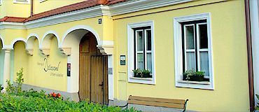 Žlutá budova s bílými okenními rámy a dřevěnými dveřmi.