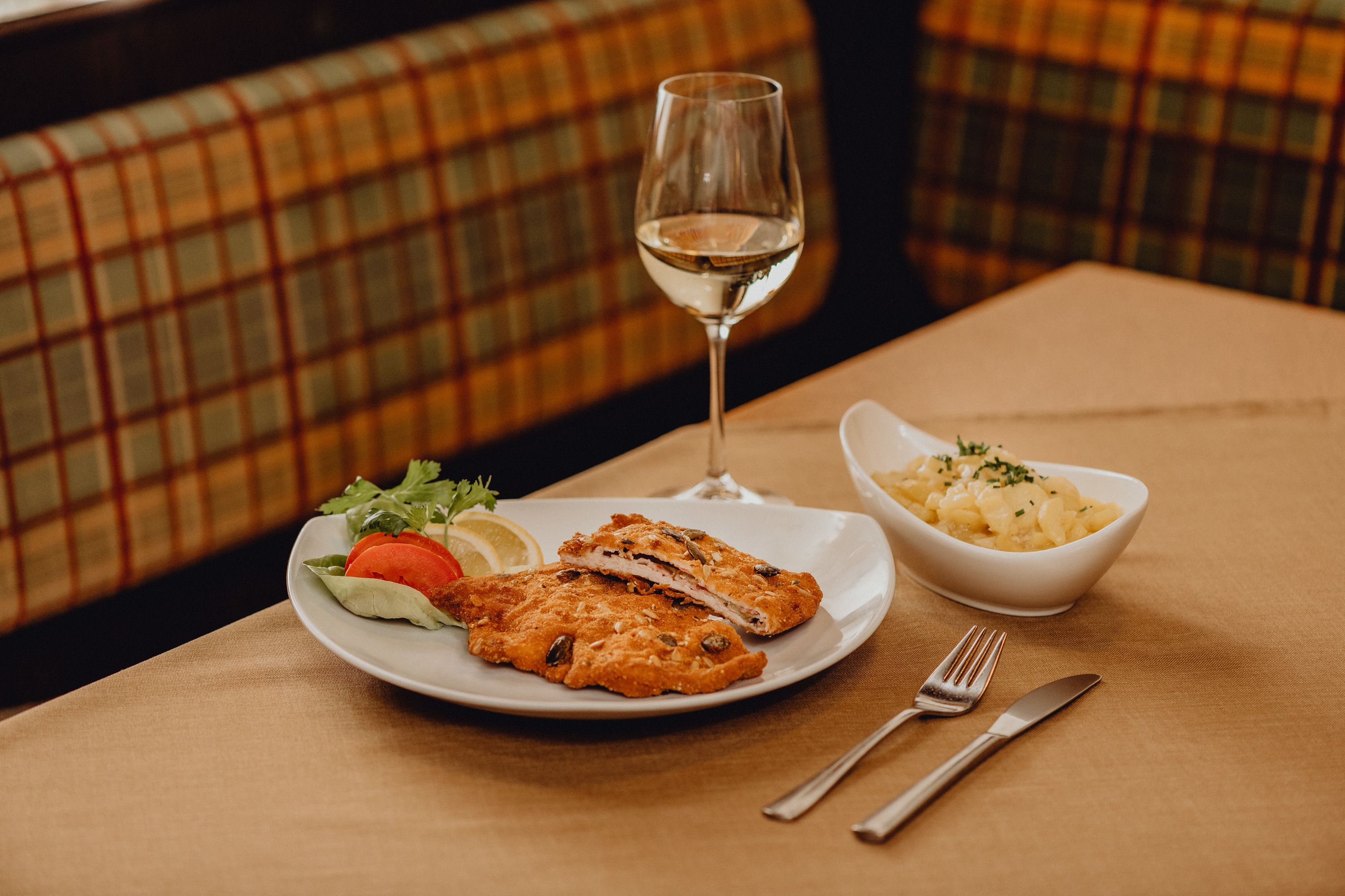 Talíř cordon bleu, salátová obloha a sklenka bílého vína na stole.