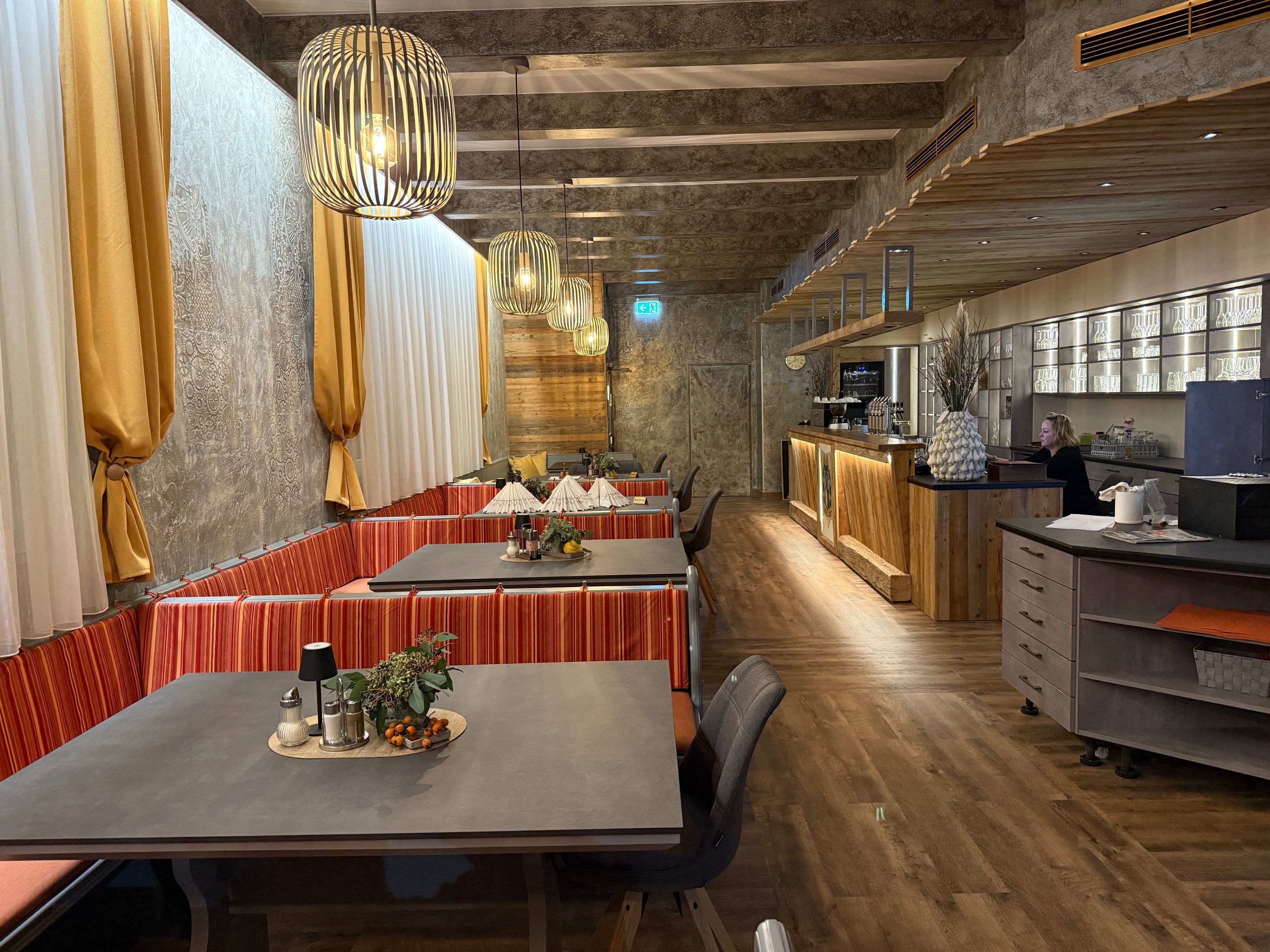 Pohled do interiéru stylové restaurace s dřevěnými prvky a moderním osvětlením.